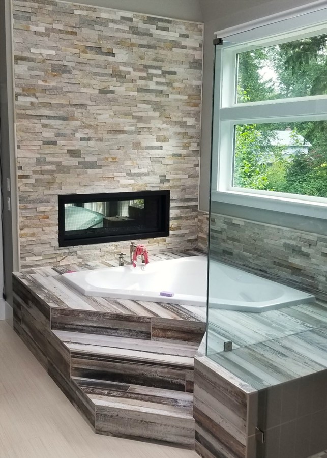 Corner soaking tub with ledgestone accent wall and wood-look plank tile