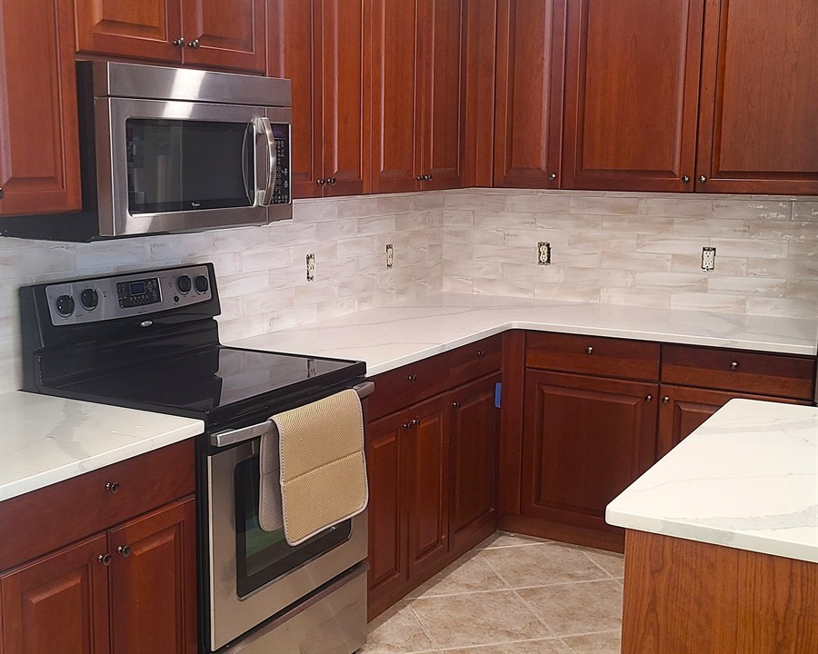 Marble-look linear tile backsplash in a cherry-cabinet kitchen